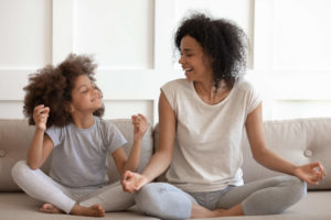 Mom and a daughter sitting cross-legged on a couch.