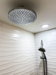 Waterfall showerhead in a shower with wavy-textured walls.