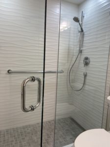 A glass shower with gray subway tile, silver hardware, and wavy walls.