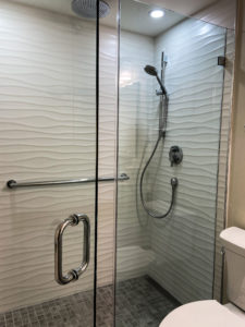 A frameless glass shower with a white wave-textured tile on the walls.