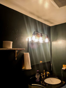 Updated bathroom with dark green walls, gold hardware, and antique-style vanity.