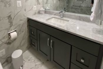 Bathroom with marble counters, marble tile floors, and dark cabinets.