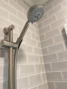 A close-up of the showerhead in a gray tiled shower.
