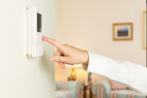 Person's hand pressing button on a white thermostat on wall of a home.