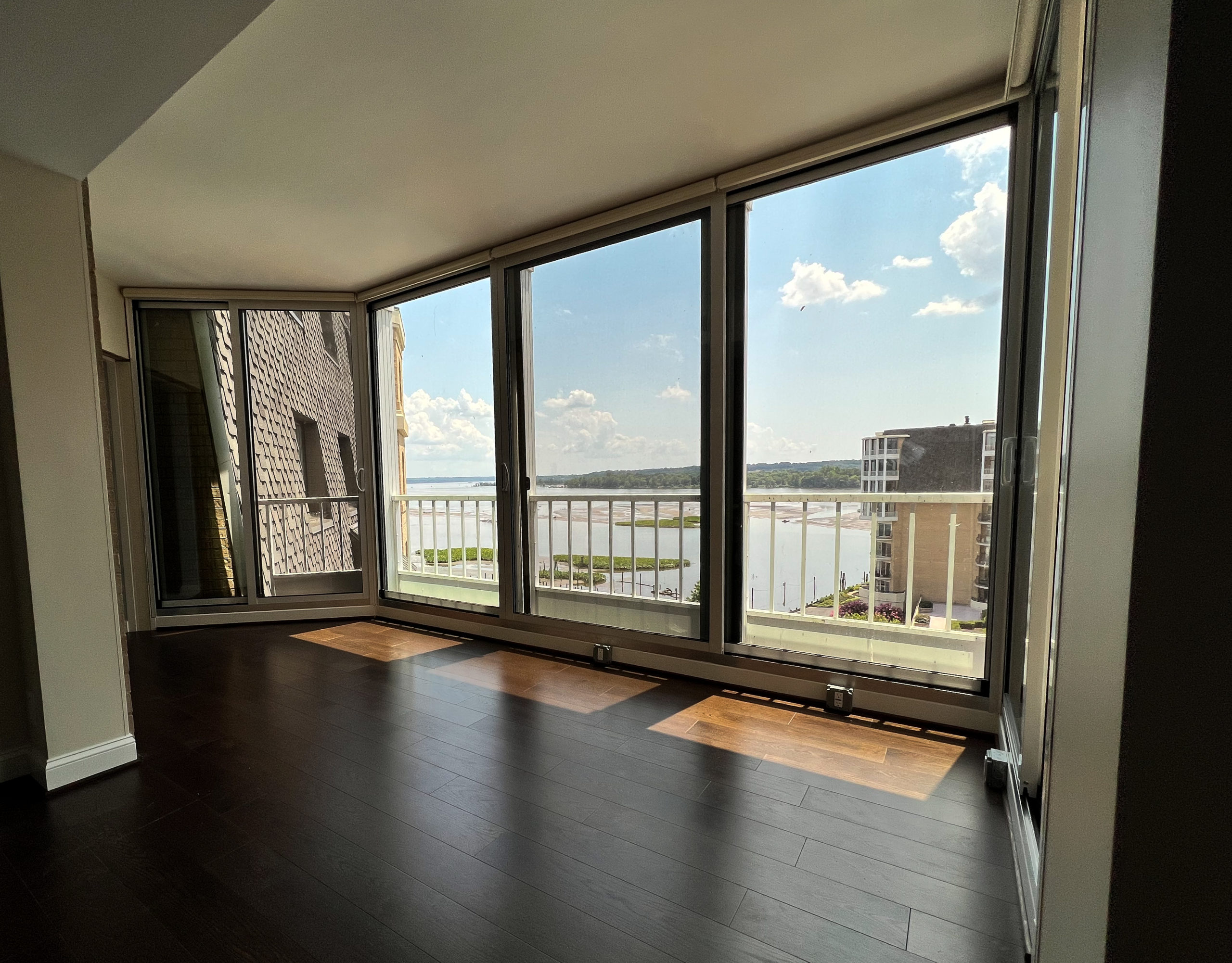 A room with dark wooden flooring and a wall of floor-to-ceiling windows.