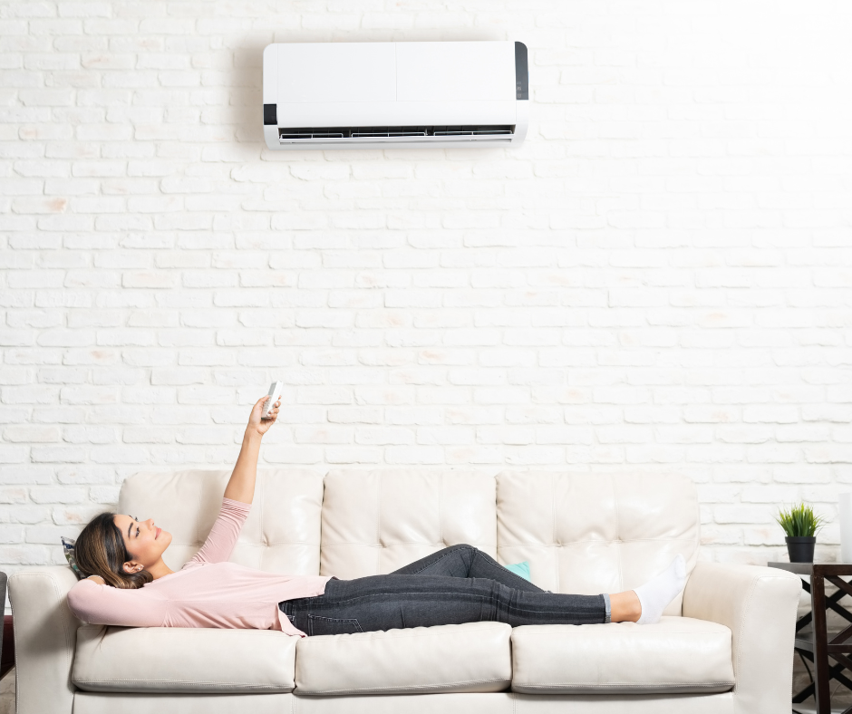 A woman lies on her couch while using a remote control to to turn on her ductless mini-split 