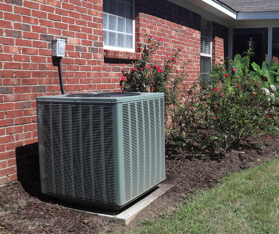 An HVAC Unit outside of a home that has fresh grass and flowering plants, insinuating that it's spring 