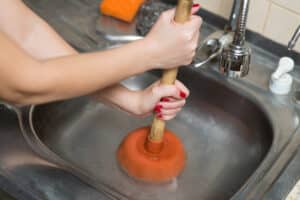 female hands apply plunger to the kitchen sink