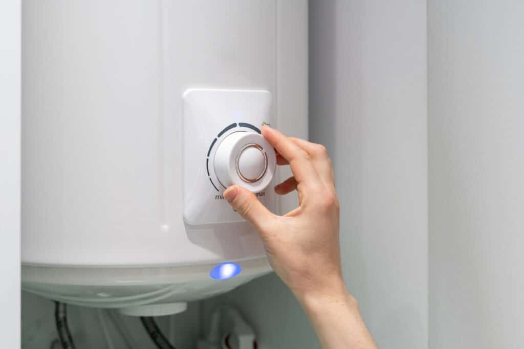 A person's hand adjusting a knob on a white boiler.