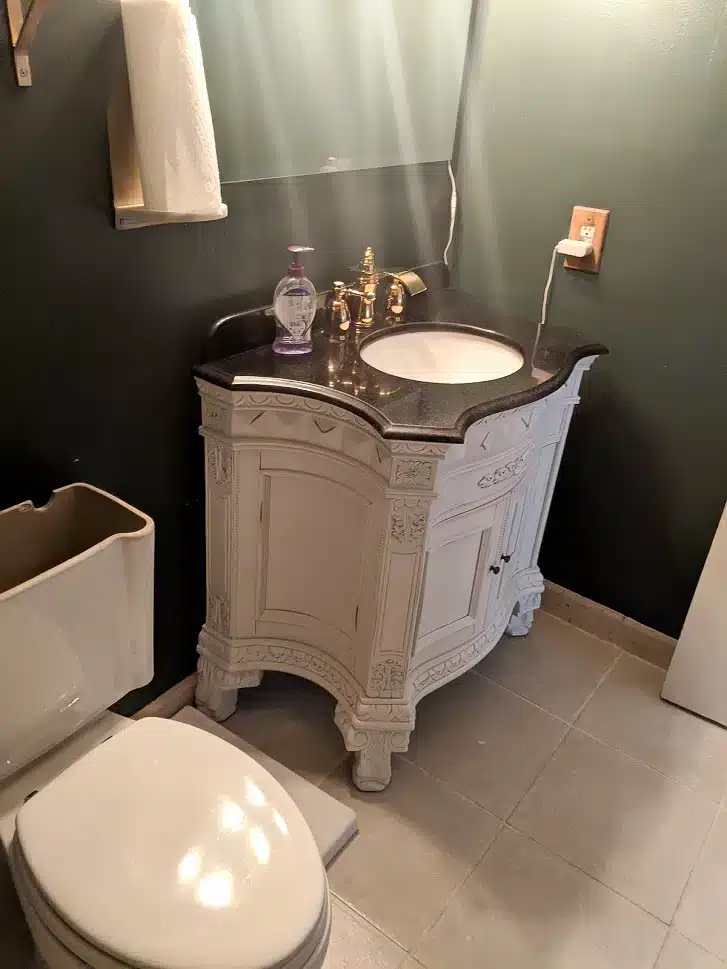 Updated bathroom with dark green walls, gold hardware, and antique-style vanity.